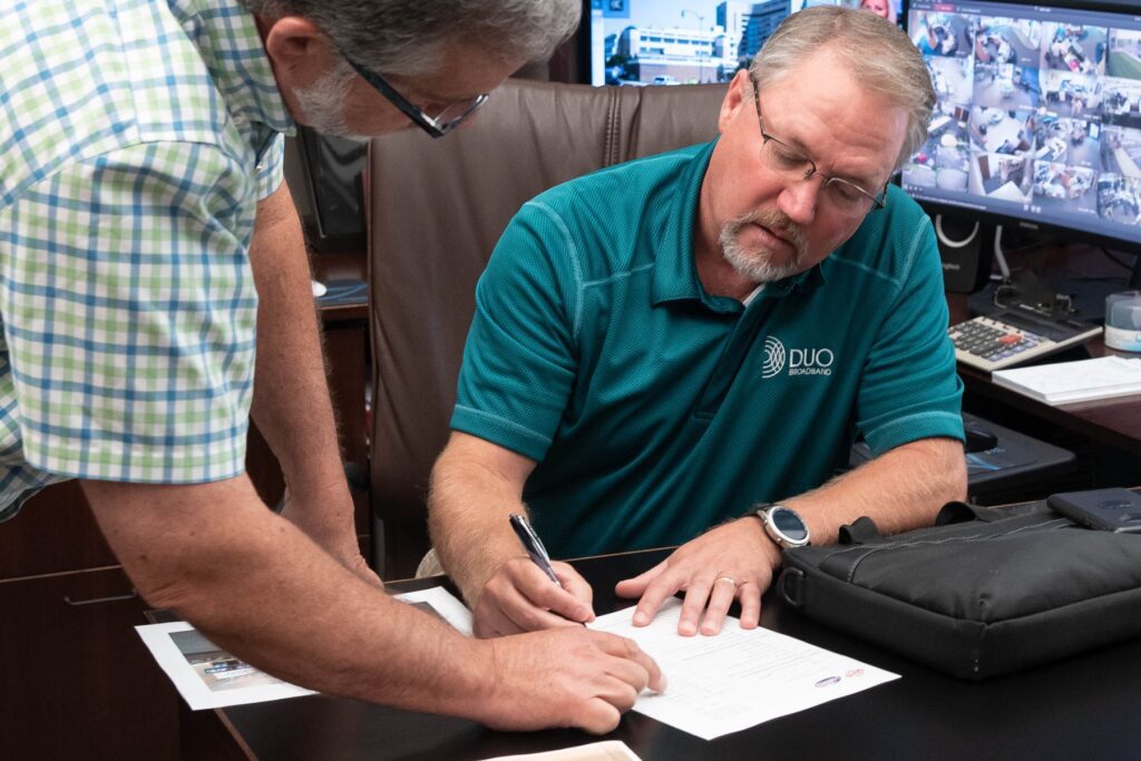 Man signing paper with DUO Broadband logo on his shirt