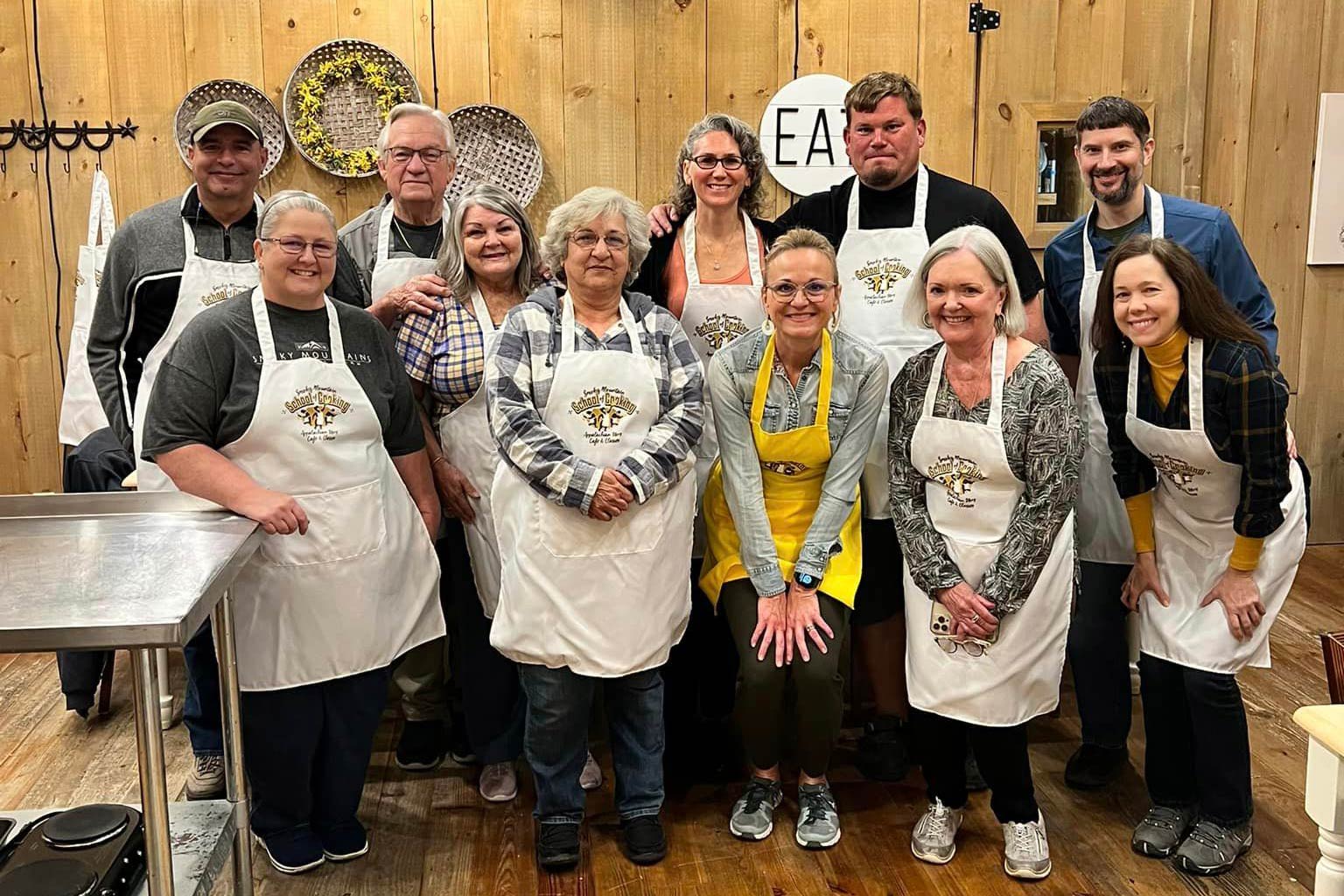 Group of smiling people posing for photo with Smoky Mountain School of Cooking branded aprons