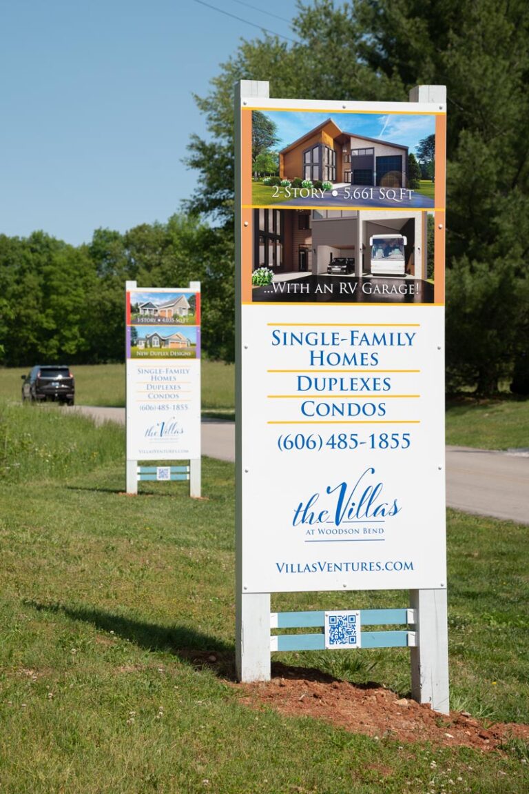 Marketing sign by the road with pictures of houses and text: Single-Family Homes, Duplexes, Condos, 606 485-1855, villasventures.com