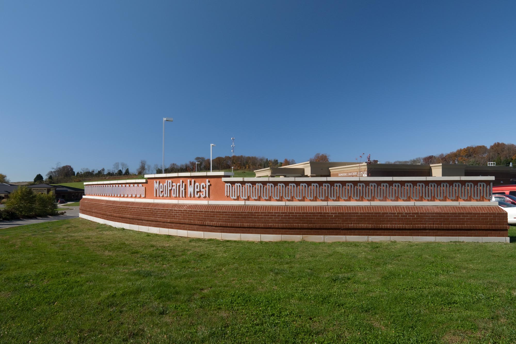 Long curving sign with brick base, MedPark West type and MedPark West symbol repeated as a pattern across the length of the structure.