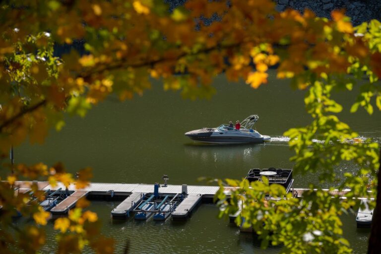 Boat cruising past a dock with fall foliage.