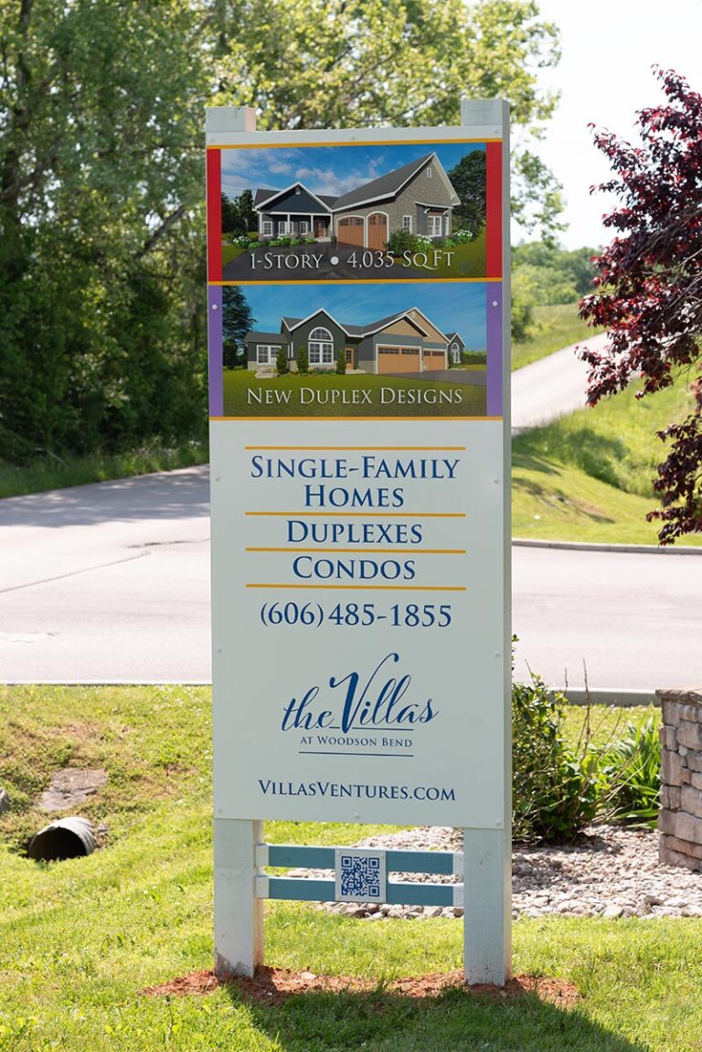 Marketing sign by the road with pictures of houses and text: Single-Family Homes, Duplexes, Condos, 606 485-1855, villasventures.com