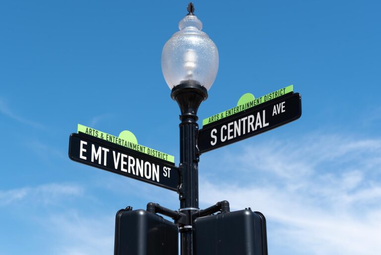 Two bladed street sign near top of lamp post that says "Arts & Entertainment District, E Mt Vernon St and S Central Ave"