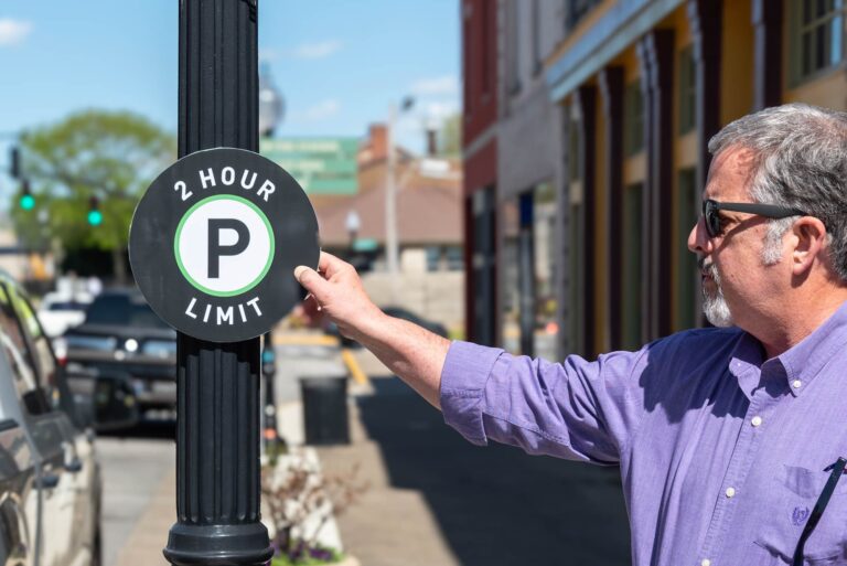 Man holding "2 hour limit" parking sign mockup up to lamp post.