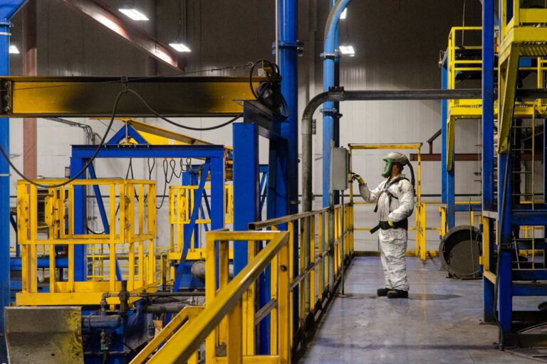 Factor worker in full body personal protective suit setting machinery on factory platform.