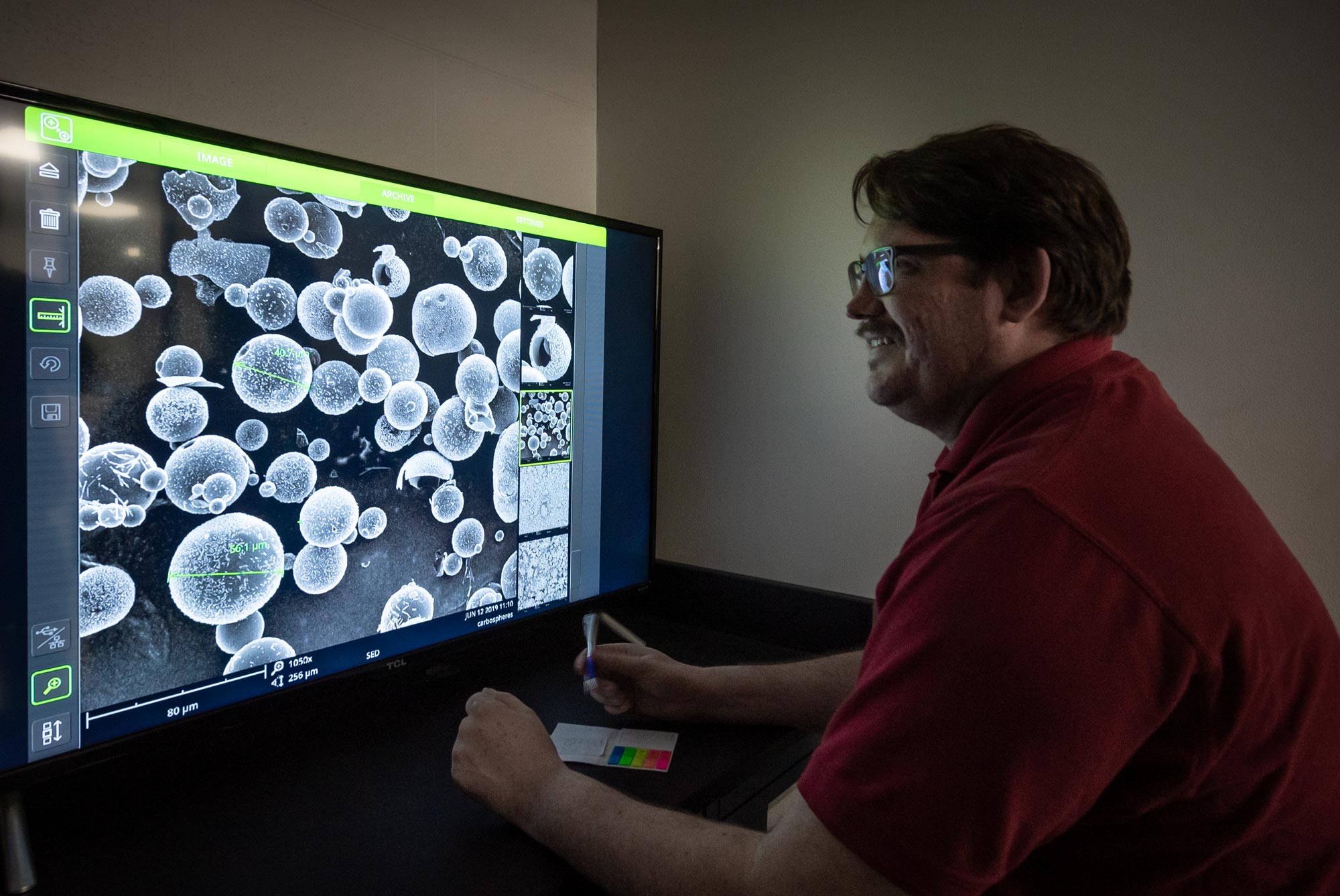 Man at computer screen showing microcopic images of chemical particles.