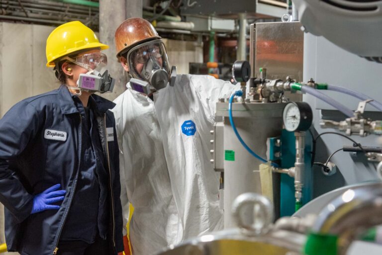 Workers in personal protective gear working with machinery in a factory environment.