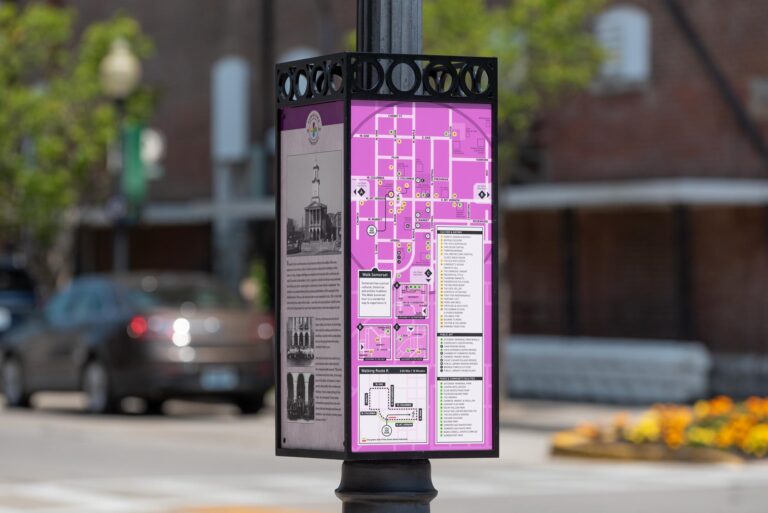 Small information sign in a box shape mounted around a lamp post.