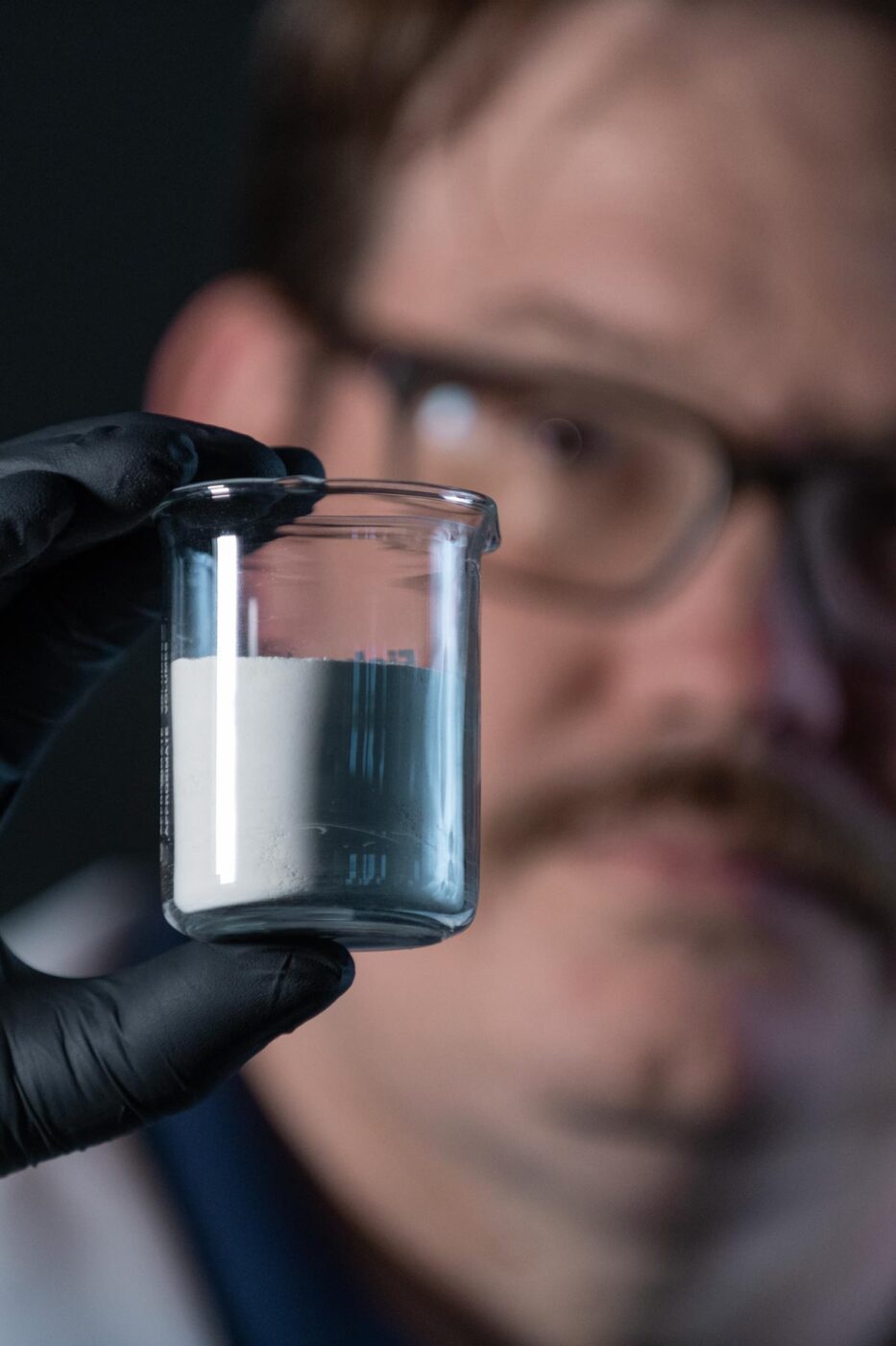 Close up of man looking at powdered chemical in lab vile.