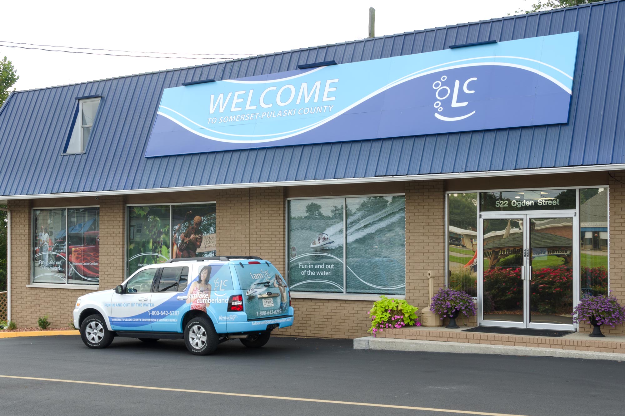 Building with large Welcome sign and photographs on the windows plus branded vehicle parked in front.