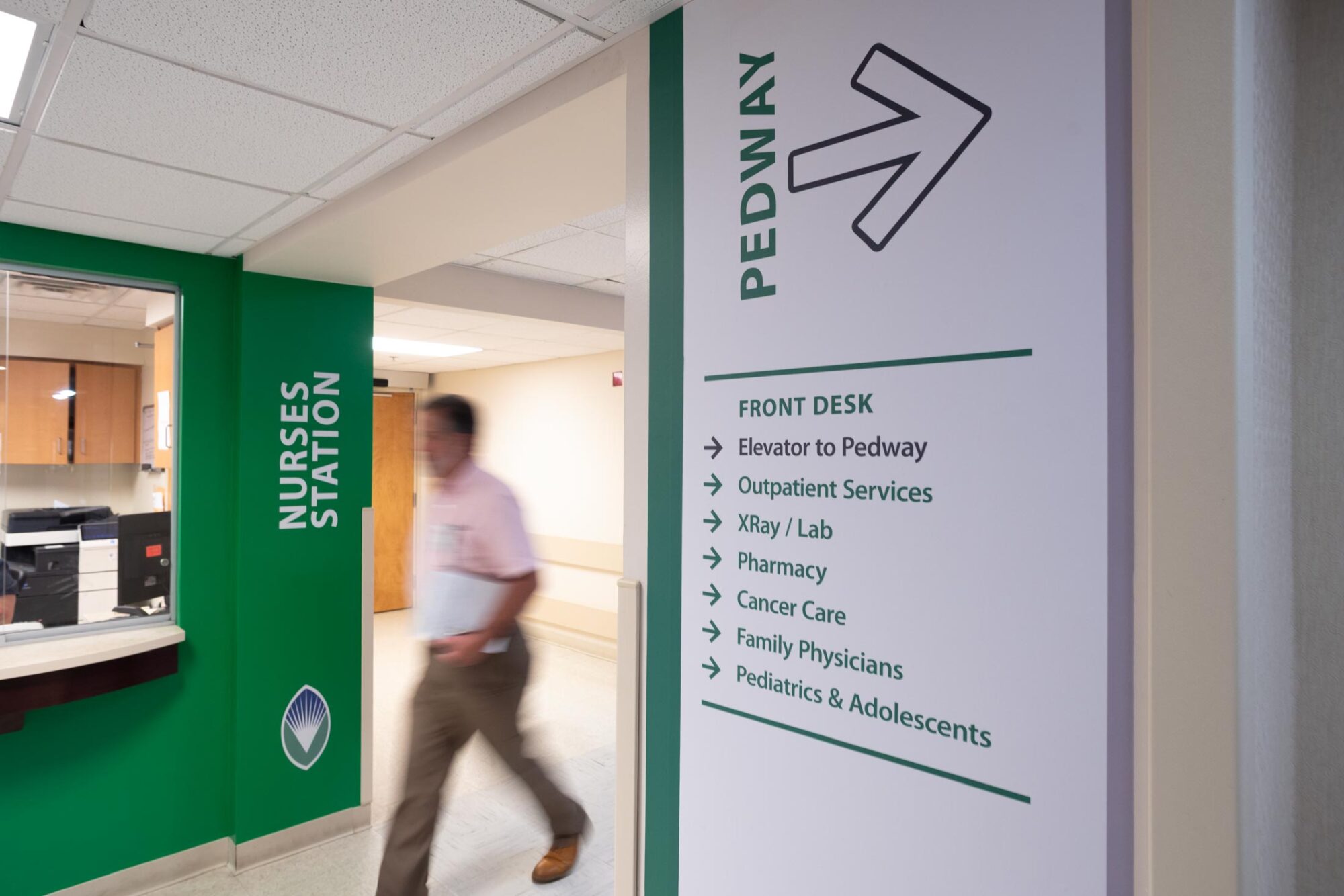 man walking in hospital corridor with directional signage onthe walls