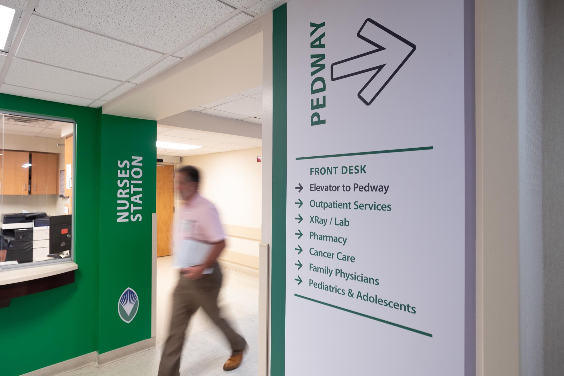 man walking in hospital corridor with directional signage onthe walls