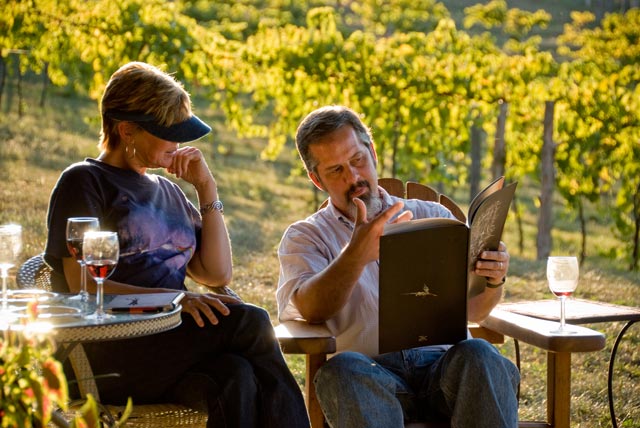 Two people in a vineyard with wine.