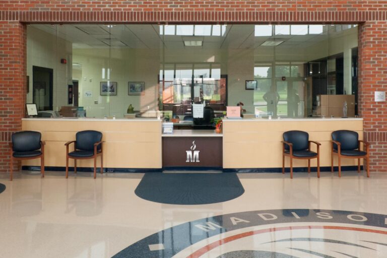 School lobby with office widow and Madison County Schools logo symbol on the wall