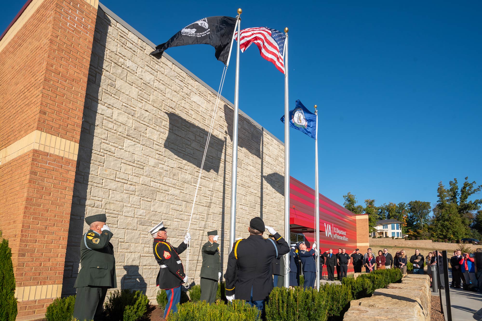 Military men raising flags in front of a VA building