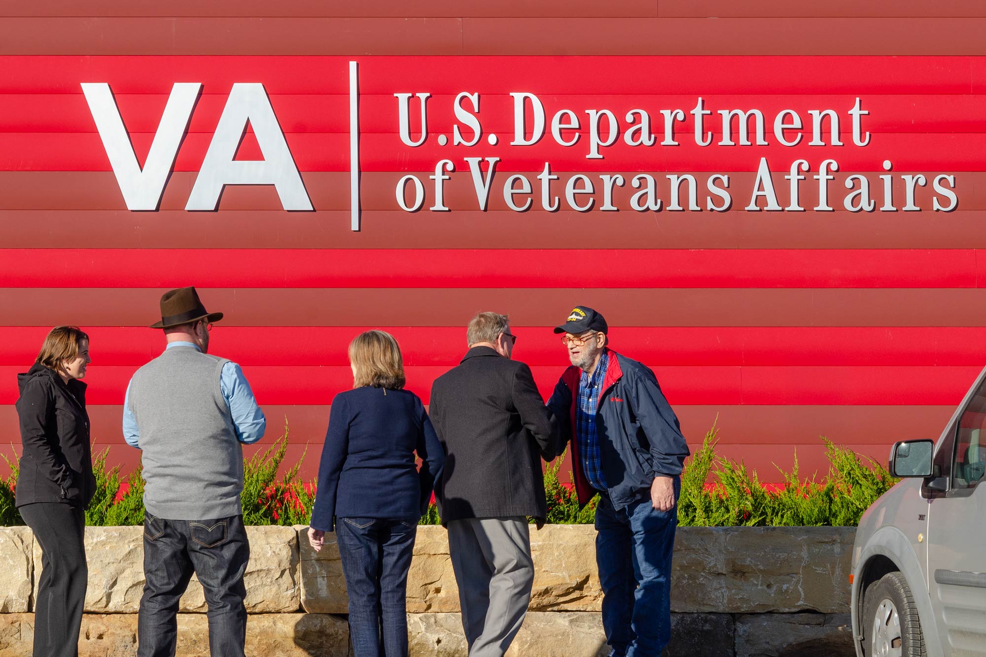People talking and shaking hands in front of a large VA U.S. Department of Veterans Affairs sign