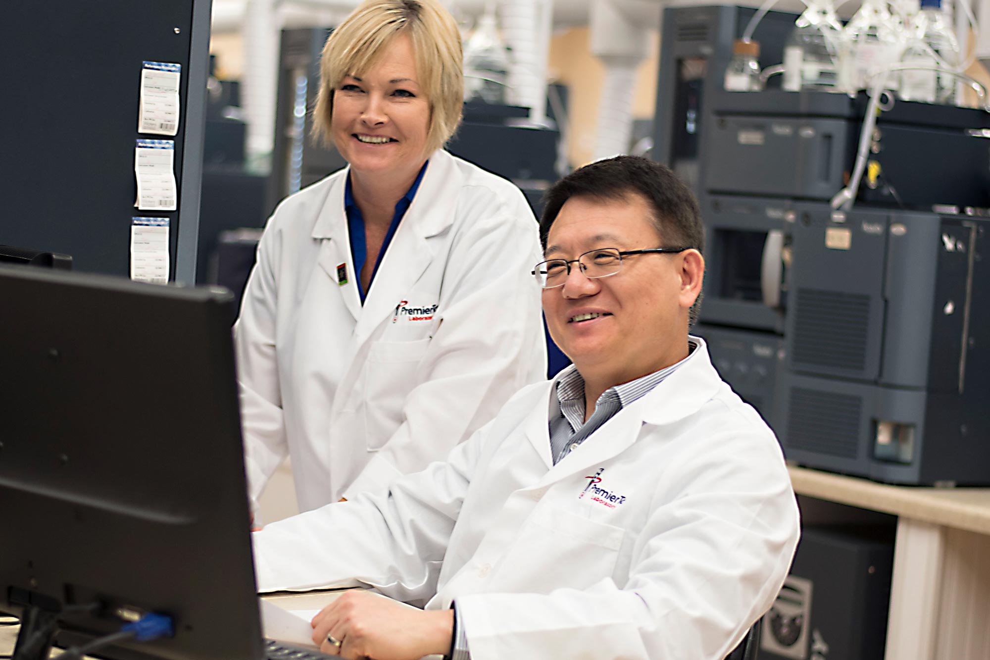 Lab techs at a computer wearing Premier Tox branded lab coats