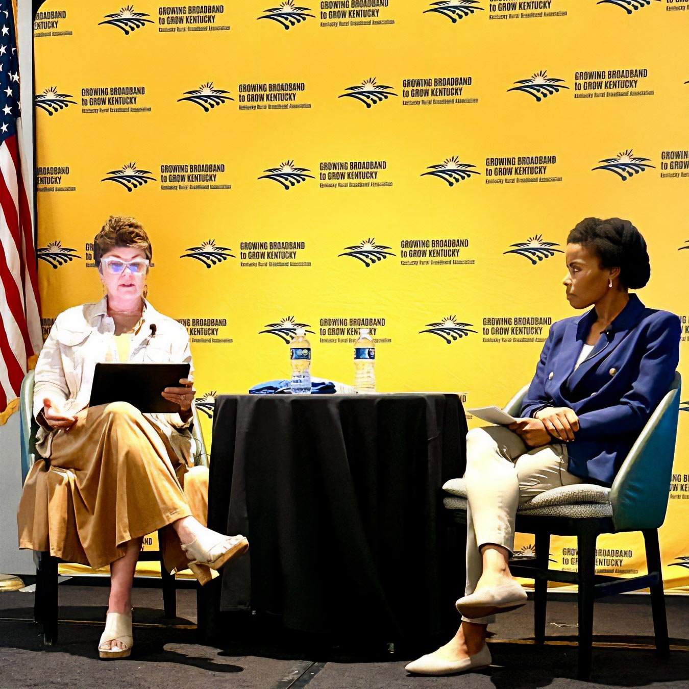 two women on stage with a Kentucky Rural Broadband Association backdrop