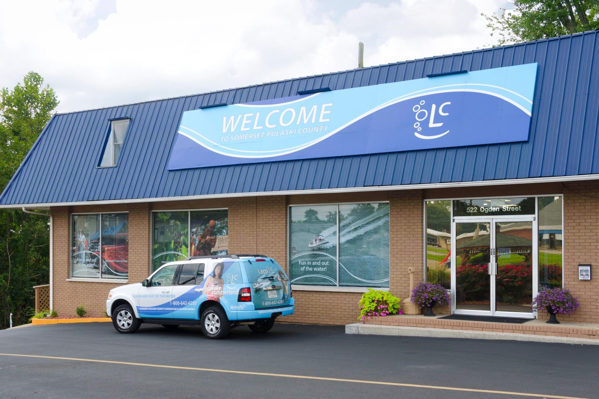 Building with large Welcome sign and photographs on the windows plus branded vehicle parked in front.
