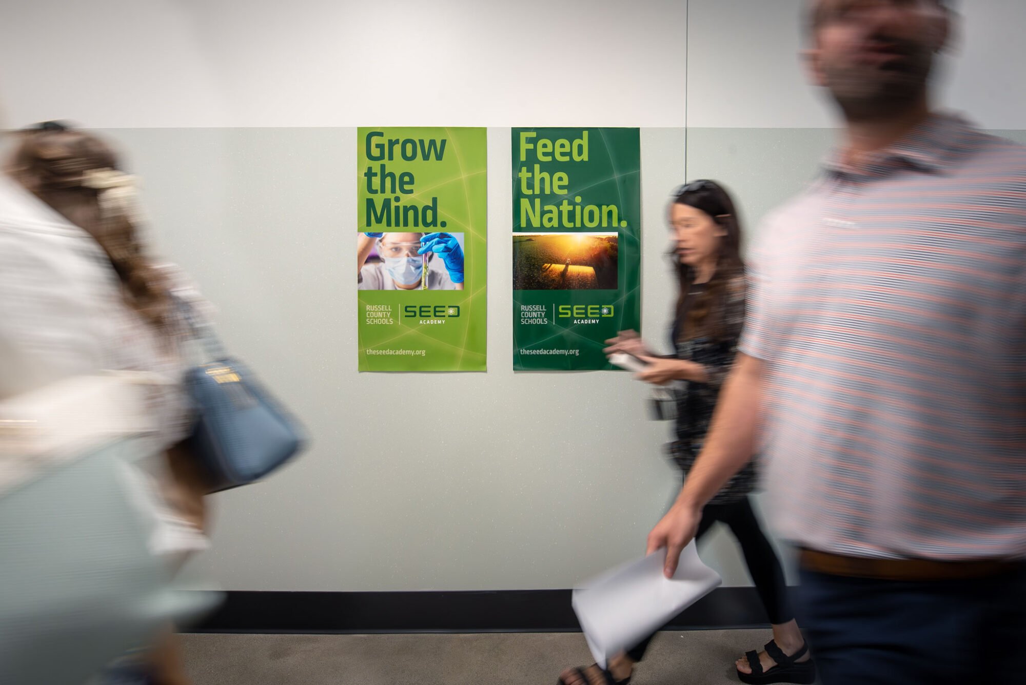 SEED Academy posters on a hallway wall with people walking past