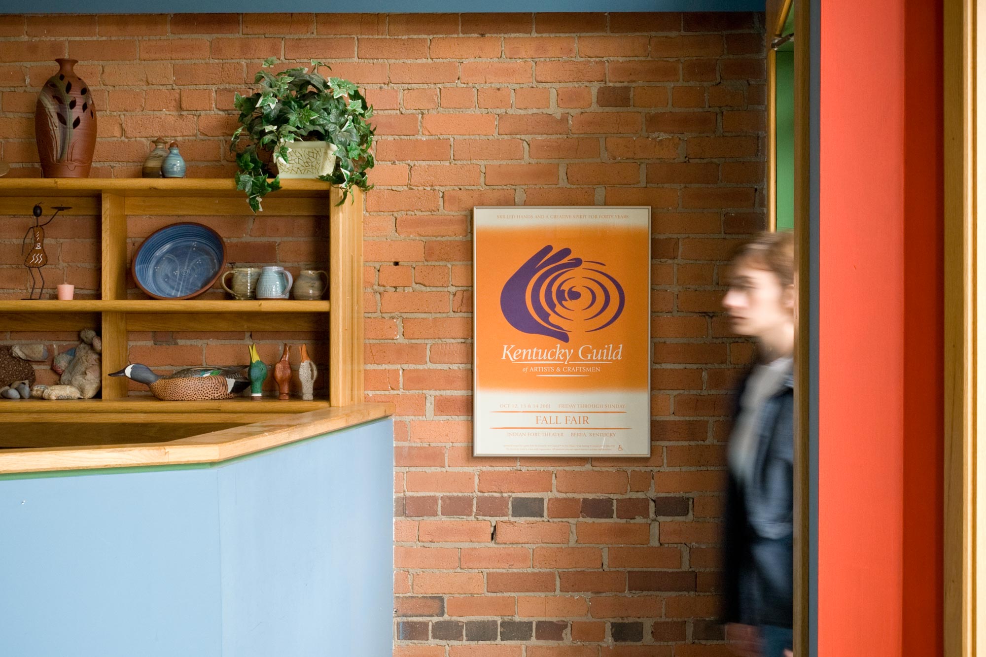person walking into a crafts shop with a Kentucky Guild of Artist & Craftsmen Guild poster on the wall