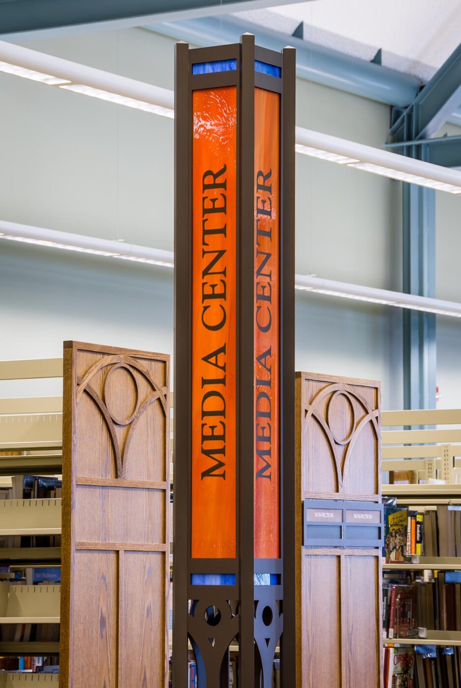 Library interior with tall, thin metal and stained glass section sign.