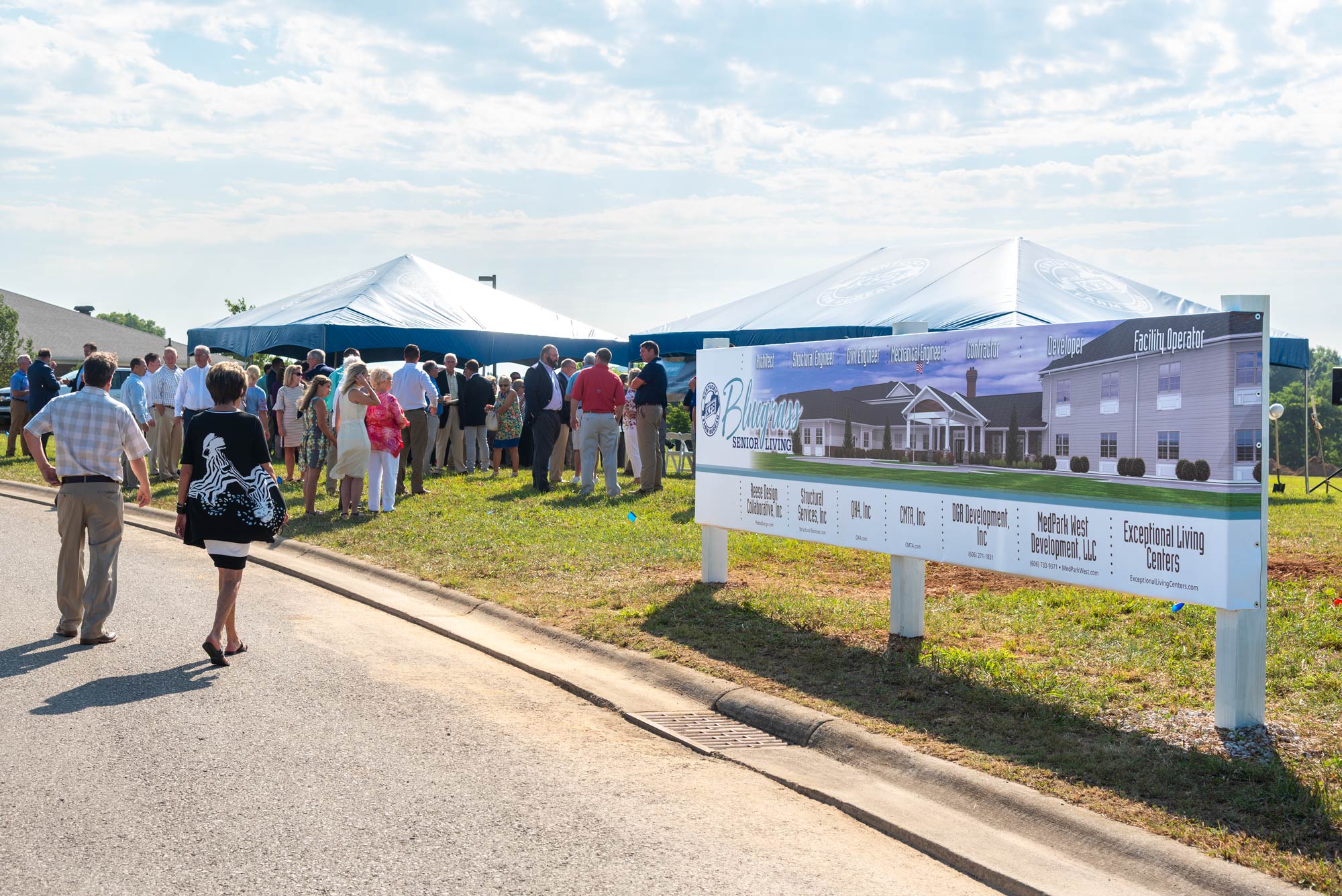 Crowd of people outdoors by tents with a large temporary sign for Bluegrass Senior Living