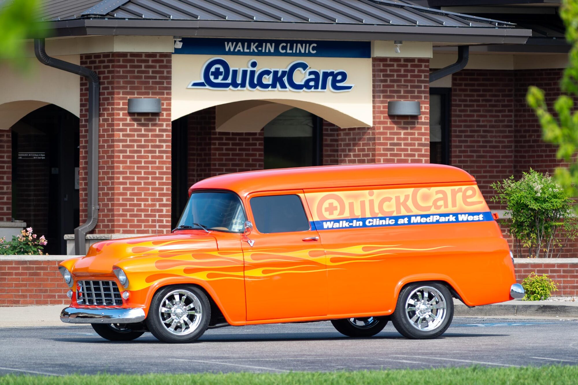 Quick Care antique van with brand graphics in front of Quick Care Walk-in Clinkc building sing
