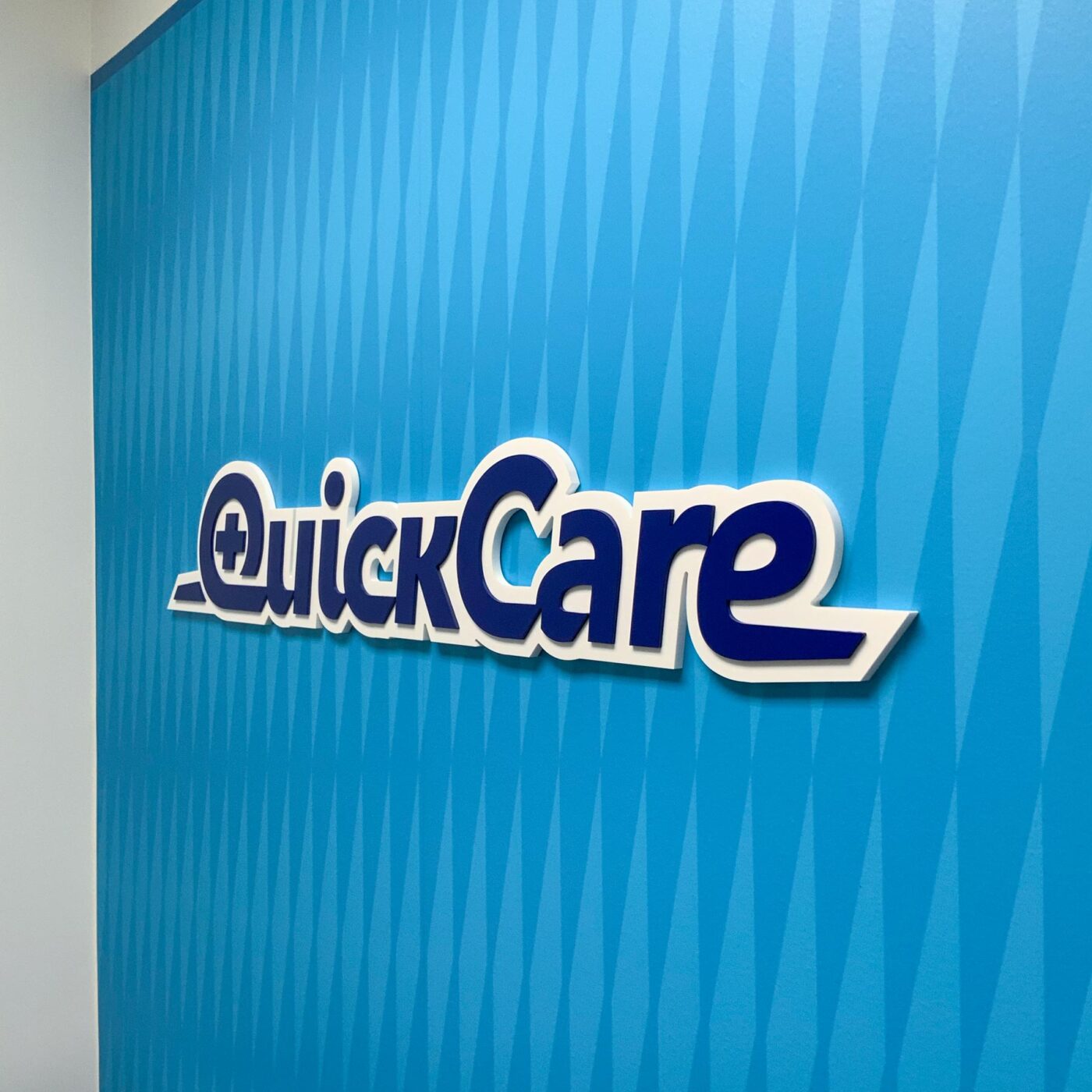 QuickCare dimensional logo on a graphic pattern wall inside the office.